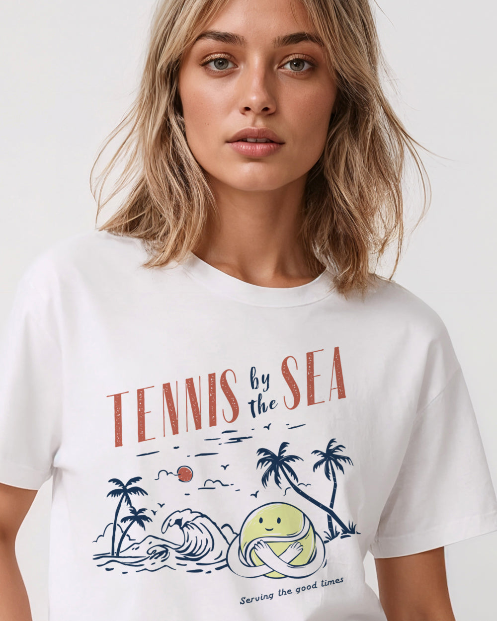 Woman wearing a white t-shirt with 'Tennis by the Sea' design on a plain background